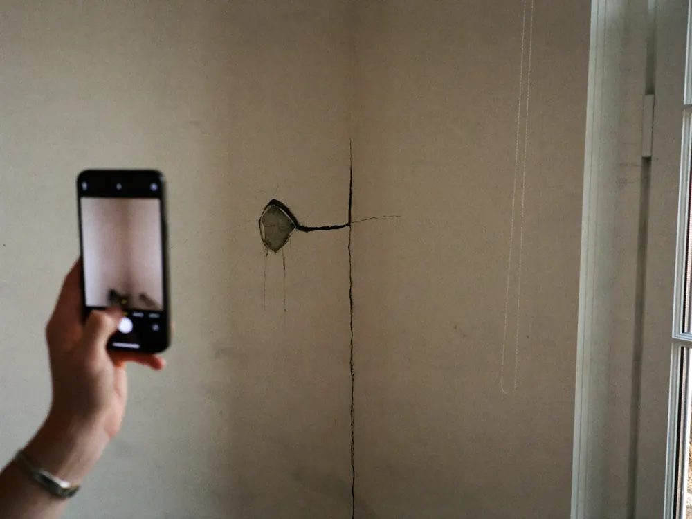 Iemand maakt met een telefoon een foto van een scheur in de muur